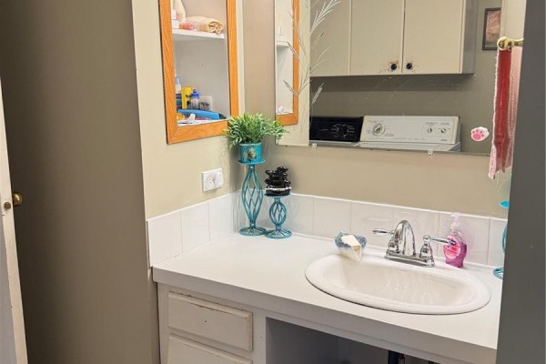 Bathroom vanity with white countertop, sink, mirror, and storage cabinets. - 316 4th Street, Weyburn