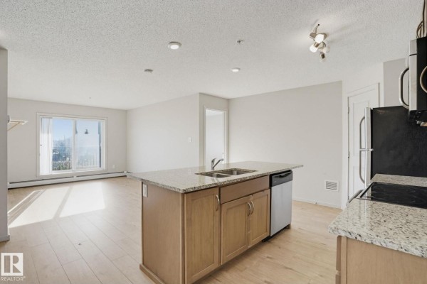 Open concept living area with light wood floors, a kitchen island with granite countertops, and a large window. - #316 7711 71 St Nw, Edmonton