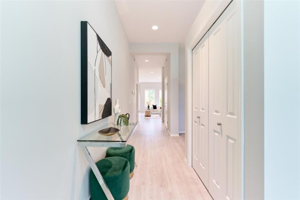 Interior view of a hallway with light wood floors, white doors, and modern artwork. - 316 Creekside Road, Winnipeg