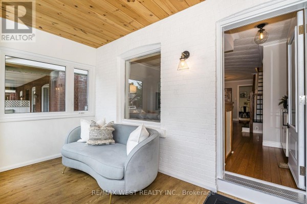 Sunroom with grey sofa, white brick walls, wood ceiling, and hardwood floor. - 316 Monarch Park Avenue, Toronto
