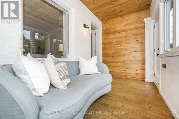 Sunroom with a grey sofa, white brick walls, wood paneling, and hardwood floor. - 316 Monarch Park Avenue, Toronto