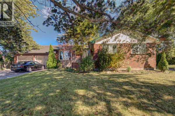 Front view of a red brick bungalow with a white-sided gable end and a large green lawn. - 3160 Binbrook Road, Binbrook