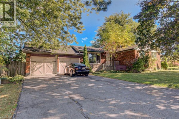 Driveway leading to a two-car garage attached to a red brick bungalow, with a black sedan parked on the asphalt. - 3160 Binbrook Road, Binbrook