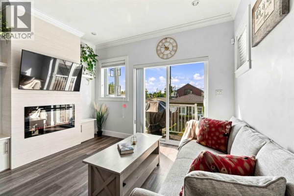 Living room with a grey sectional sofa, coffee table, fireplace, and sliding glass doors. - 3162 Venables Street, Vancouver
