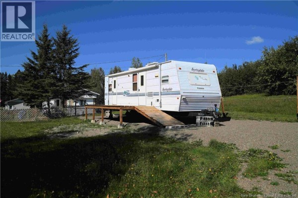 White RV trailer with wooden ramp on gravel pad, surrounded by green grass and trees. - 3164 Route 108, New Denmark
