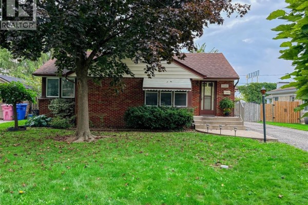 Front view of a red brick bungalow with a green lawn and mature tree. - 3168 Church, Windsor