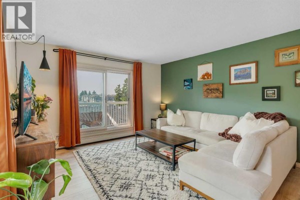 Living room with a sectional sofa, rug, entertainment unit with TV, and window with view. - 317, 2211 29 Street Sw, Calgary