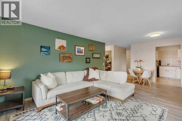 Living room with a sectional sofa, green accent wall with art, and doorway to dining area. - 317, 2211 29 Street Sw, Calgary