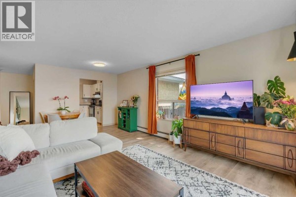 Living room with a sectional sofa, dining area, and kitchen area visible in background. - 317, 2211 29 Street Sw, Calgary