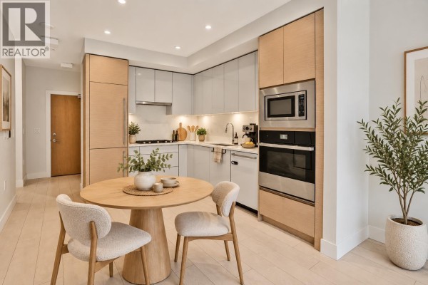 Compact kitchen with light wood cabinetry, stainless steel appliances, and a small round dining table. - 317 3438 Sawmill Crescent, Vancouver