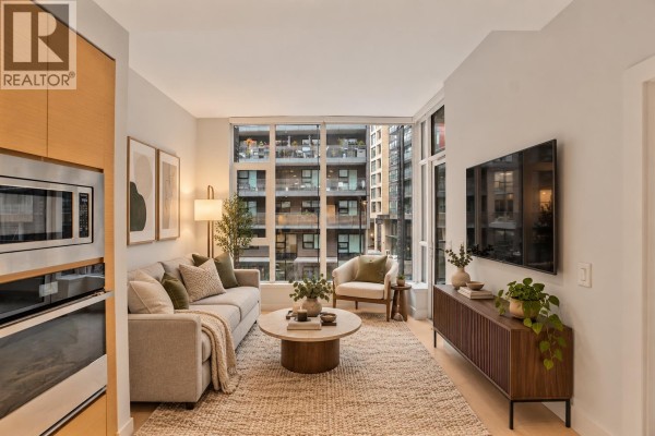 Living room with a grey sofa, coffee table, armchair, and television against a large window. - 317 3438 Sawmill Crescent, Vancouver