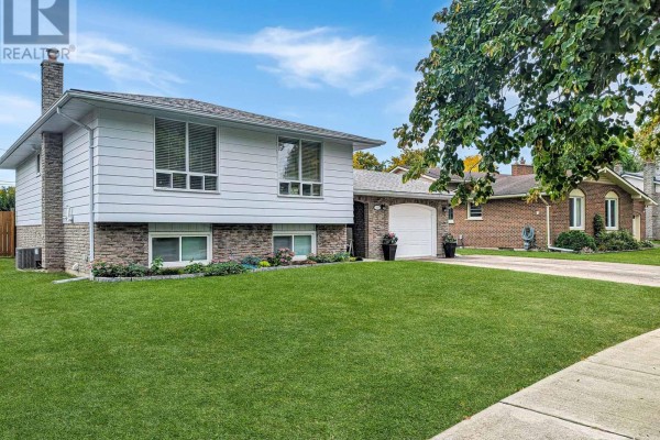 Side exterior view of the raised bungalow showing white siding, stone accents, and a manicured lawn. - 3170 Corry Crescent, Niagara Falls