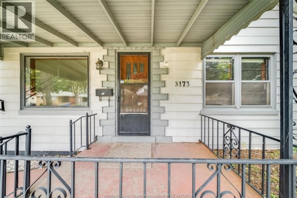 Close-up of the covered front porch entrance with a black door, mail slot, and brick accents. - 3173 Wyandotte St West, Windsor