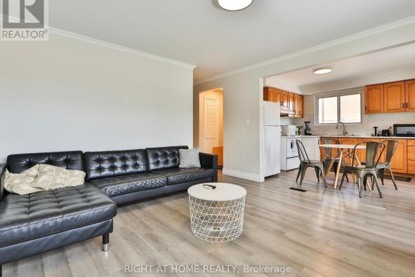 Living room with black sectional sofa, coffee table, and view of the kitchen. - 3174 Weston Road, Toronto
