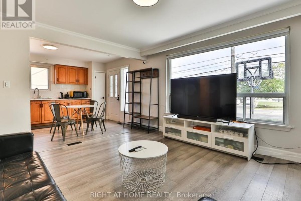 Living room with large window, television, and adjacent kitchen and dining area. - 3174 Weston Road, Toronto