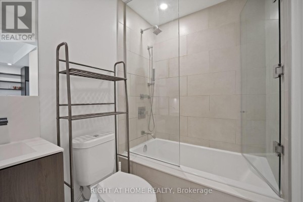 Modern bathroom with a soaking tub, glass shower doors, and tiled walls. - 318 - 12 Bonnycastle Street, Toronto