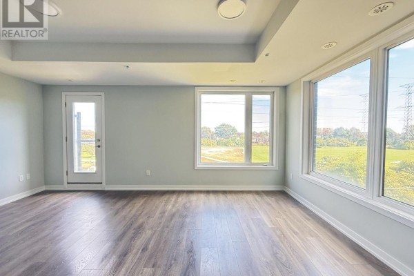 Living room with large windows and a door opening to a balcony. - 318 - 1555 Kingston Road, Pickering