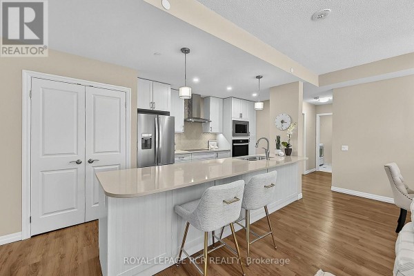 Modern kitchen with white cabinets, island, stainless steel appliances, and pendant lights. - 318 - 460 William Graham Drive, Aurora