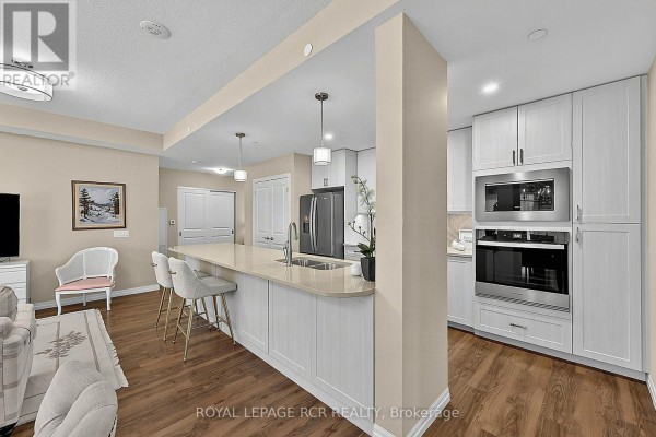 View of the kitchen island, breakfast bar with stools, and living room area. - 318 - 460 William Graham Drive, Aurora