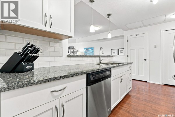 Kitchen island with granite countertop, white subway tile backsplash, stainless steel dishwasher, and sink. - 318 1220 Blackfoot Drive, Regina