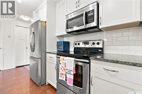 Kitchen detail showing stainless steel appliances, granite countertop, white cabinets, and hardwood flooring. - 318 1220 Blackfoot Drive, Regina