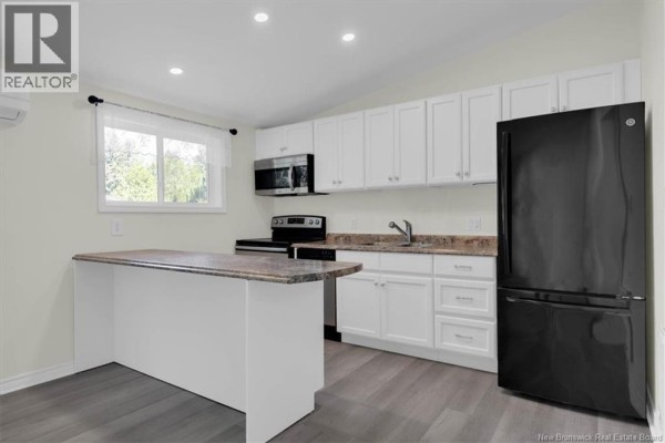 Kitchen with white cabinets, black appliances, a granite countertop island, and grey wood-look flooring. - 318 Parr Street, Saint Andrews