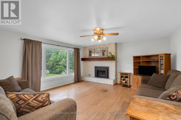 Living room with a brick fireplace, hardwood floors, and a large window overlooking the trees. - 318 Percy Street, Tay