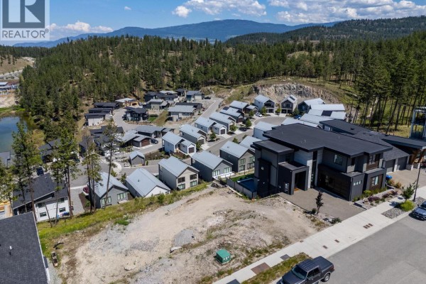 Aerial view of a hilly development with modern houses, a vacant lot, and a pond. - 3183 Hilltown Drive, Kelowna