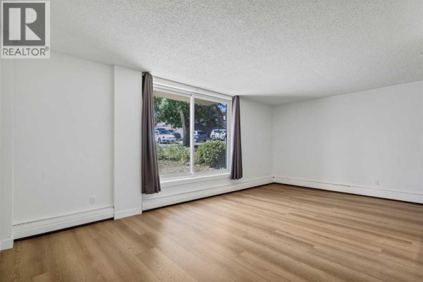Living room and kitchen area with white walls, large window, and wood-look flooring. - 319, 315 Heritage Drive Se, Calgary