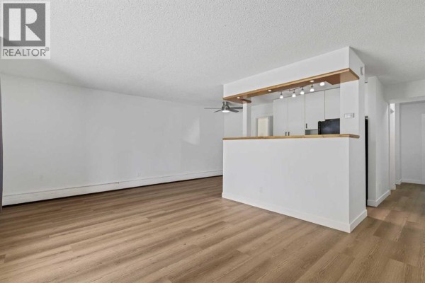 Empty living room with white walls, wood-look flooring, and a large window view. - 319, 315 Heritage Drive Se, Calgary