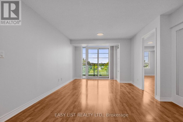 Empty living room with hardwood floors, white walls, and a large window. - 319 - 2020 Mcnicoll Avenue, Toronto