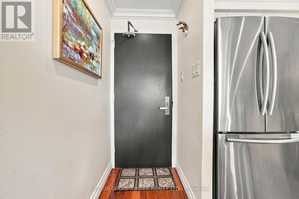 View of the apartment's entryway with a dark door, a mat, and a stainless steel refrigerator. - 319 - 35 Ormskirk Avenue, Toronto