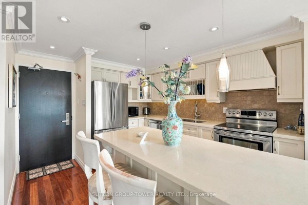 View of the kitchen and dining area with a large island, bar stools, and white cabinetry. - 319 - 35 Ormskirk Avenue, Toronto