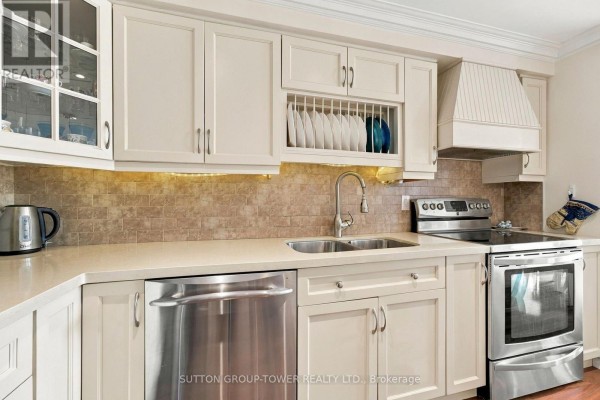 Close-up of the kitchen sink, stainless steel dishwasher, and stove with cream-colored cabinets. - 319 - 35 Ormskirk Avenue, Toronto