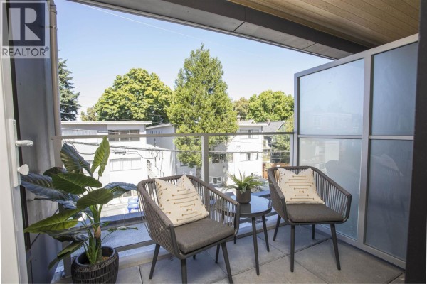 Balcony with two chairs, a small table, and a view of trees and buildings. - 319 2471 St. George Street, Vancouver