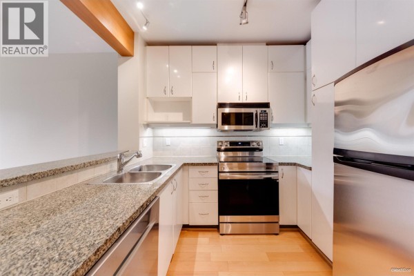Corner kitchen with white cabinets, granite counters, stainless steel appliances, and a double sink. - 319 580 Raven Woods Drive, North Vancouver