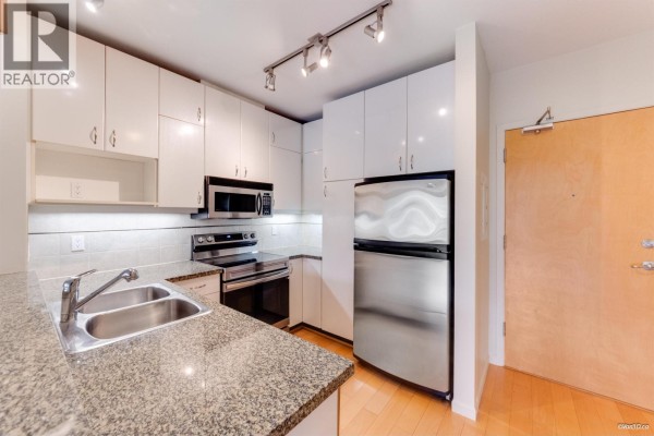 Kitchen with white cabinets, granite counters, stainless steel appliances, and a wood door. - 319 580 Raven Woods Drive, North Vancouver