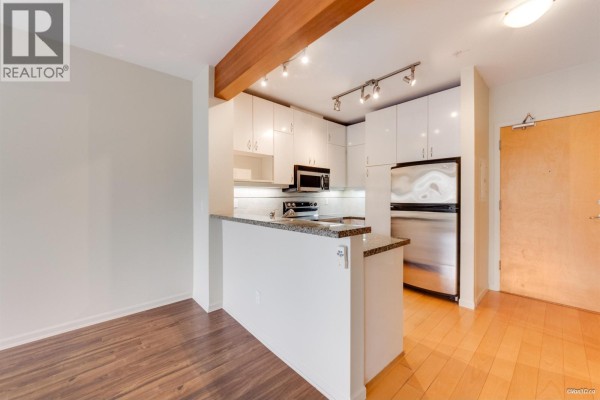 Kitchen with white cabinets, granite counter peninsula, stainless steel appliances, and adjacent living area. - 319 580 Raven Woods Drive, North Vancouver