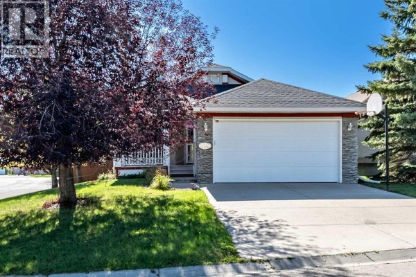 Front exterior of a beige house with a stone-accented garage door and a basketball hoop in the driveway. - 319 Cimarron Bay, Okotoks