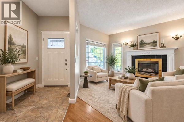 Entryway with tiled floor and white door, opens to a living room with a fireplace and light-colored furniture. - 319 Cimarron Bay, Okotoks
