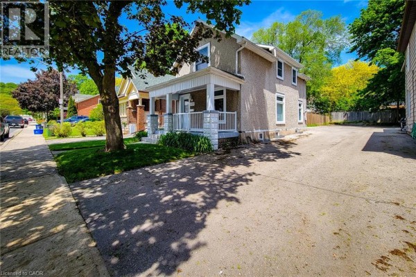 Side exterior of a house showing a paved driveway, a covered porch, and neighboring properties. - 319 King Street W, Dundas