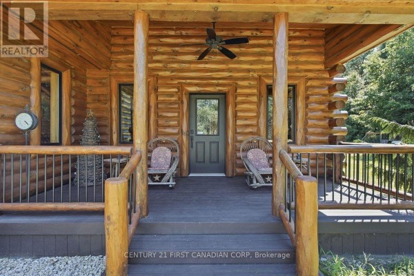 Front porch of the log cabin with two chairs, a ceiling fan, and a glass-paned door. - 31998 Scout Road, North Middlesex