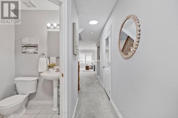 Small bathroom with a pedestal sink, toilet, vanity light, and hallway access. - 32 - 130 Robert Street, Milton