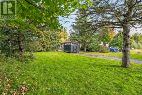 View of the mobile home from the side, with a dumpster and trees in the foreground. - 32 - 7481 Mitch Owens Road, Ottawa