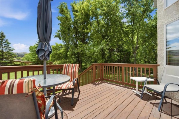 Close-up of a wooden deck with patio furniture and an umbrella, overlooking a backyard. - 32 385 Willowlake Crescent, Winnipeg