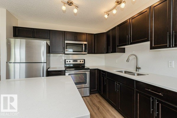 Kitchen with dark wood cabinets, white quartz countertops, stainless steel appliances, and a tiled backsplash. - #32 445 Brintnell Bv Nw, Edmonton