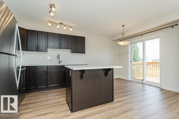 Kitchen area with dark cabinets, white island, and sliding glass doors leading to a wooden deck. - #32 445 Brintnell Bv Nw, Edmonton