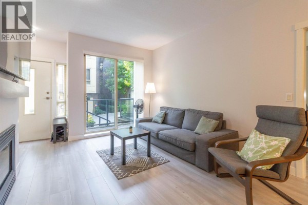Open living and dining area with a modern kitchen in the background and a cozy sofa. - 32 9229 University Crescent, Burnaby
