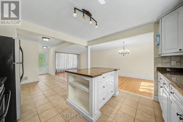 Kitchen with white cabinets, granite countertops, and a central island, overlooking the living and dining areas. - 32 Alanadale Avenue, Markham