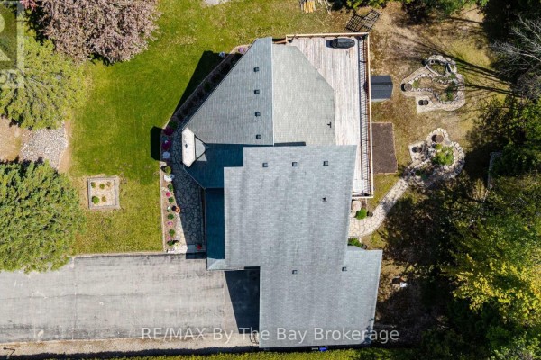 Side exterior view of a two-story home with large windows, a stone chimney, and a double garage at dusk. - 32 Bridlewood Crescent, Wasaga Beach
